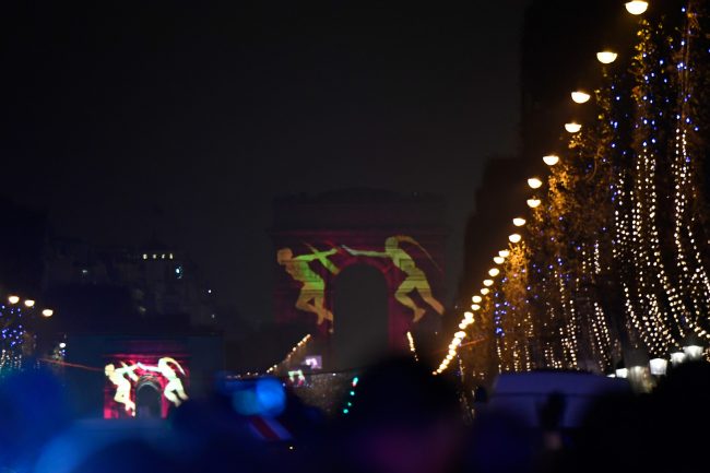 Revellers gather on the Champs-Elysees avenue to watch a laser and 3D video mapping show projected on the Arc de Triomphe monument as part of the New Year celebrations on December 31, 2016 in Paris. / AFP PHOTO / Olivier MORIN
